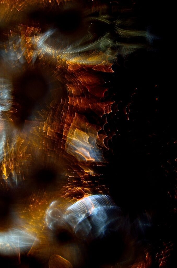 Abstract swirl of warm orange and gold bokeh lights against a dark background, resembling a kaleidoscope of sparks.